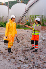 Two environmental researchers walk back from shoreline testing. They carry safety gear, a toolbox, a respirator mask, and a laptop after collecting water samples from a contaminated coast.