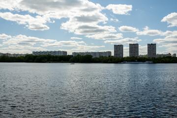 Serene View of Urban Skyline Over Tranquil River With Scattered Clouds and Lush Greenery Nearby