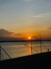 Silhouette of fishing nets and a person against a vibrant sunset over a wide river