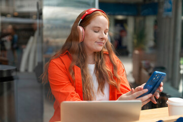Young woman enjoying music while using a smartphone in a cozy cafe during a sunny afternoon