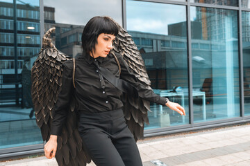 Woman wearing unique feathered wings poses in an urban environment, showcasing a blend of fashion...