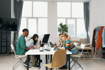 Young adult colleagues socializing and working together in a bright workplace, showcasing Gen Z friends collaborating on business tasks at a modern office environment.