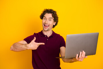 Happy man in casual burgundy polo shirt holding a laptop, showing excitement on a vibrant yellow...