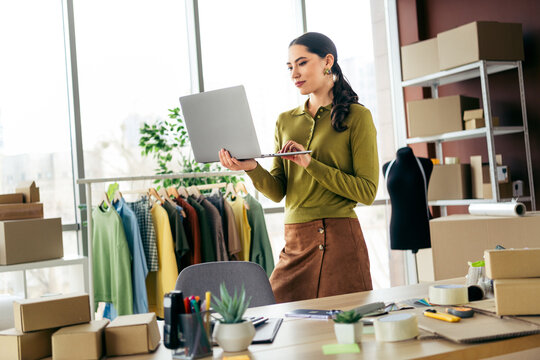 Young entrepreneur working with a laptop in a fashion studio surrounded by textiles and garments, showcasing creativity and dedication. - Powered by Adobe