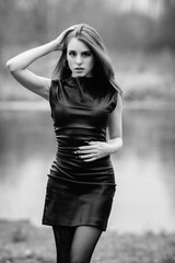 Portrait of a young beautiful dark-haired girl in a black dress outdoors. Black and white photo.