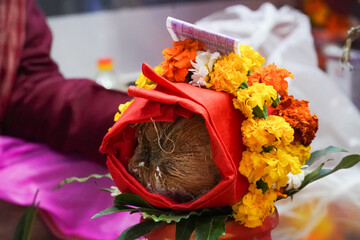 Close-up of a decorated coconut wrapped in red cloth with marigold flowers, part of a traditional Hindu ritual or puja ceremony.