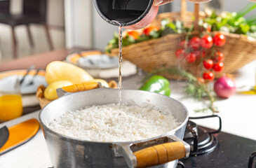 Woman pouring white rice into a frying pan with ingredients on the background.