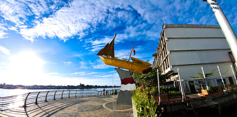 Golden boat statue on the banks of the Kapuas River with a view of bright blue sky and scattered...