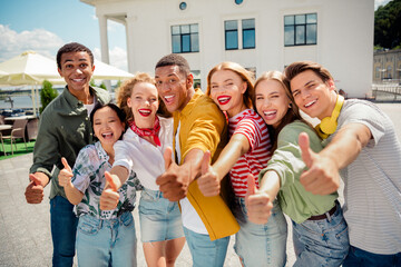 Group of cheerful young friends giving thumbs up outdoors on a sunny day symbolizing friendship and...