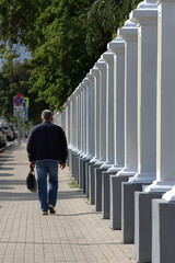 A man with a briefcase walks along the sidewalk along a stone fence