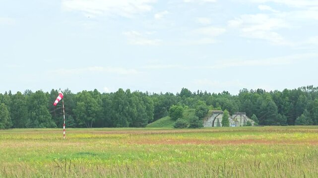 Two closed bunkers for army air-craft and red white windsock moving in the air. Closed defence airport without army.
