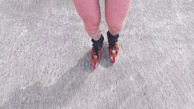 Close-up view of male legs in orange inline blades boots moving on the road. 