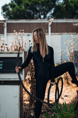 A stylish blonde woman in a black bodysuit poses barefoot on top of an old, weathered gas pump at...
