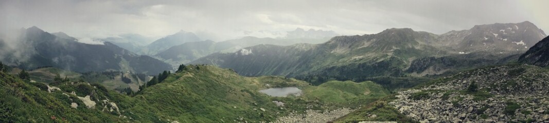 Panoramic view of a tranquil mountainous landscape with lush greenery and small lake