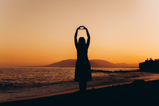 Woman making heart shape with hands at sunset on beach