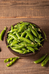 Fresh green peas and pods in a bowl on wooden table. Vegetable healthy food.  