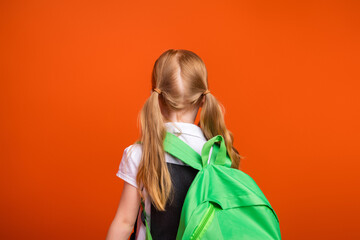 Back view of a young girl wearing a green backpack against a bright orange background representing...