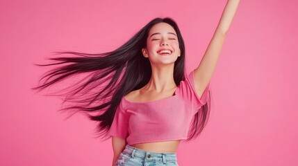 Joyful young asian woman with long brunette hair dancing against a vibrant pink background conveying happiness and freedom