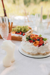 Whipped cream pavlova cake topped with fresh apricots, strawberries, berries, and mint on picnic table.	Closeup of elegant pavlova dessert with white cream peaks, orange apricots, red raspberries