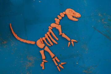 Orange clay dinosaur bones arranged into full skeleton on striking blue backdrop, showcasing...
