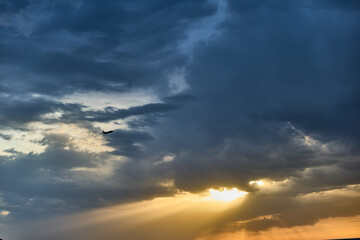 Dramatic sky with dark clouds and sun rays illuminating the horizon during sunset, emphasizing atmospheric contrast and moody natural landscape