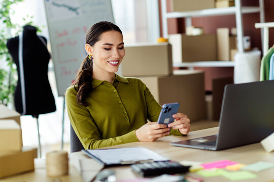 Young fashion designer working on mobile device in couture studio surrounded by materials, emphasizing entrepreneurship