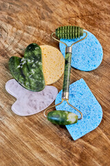 a pleasant cosmetic composition with a quartz roller, two gua sha pink and green and three sponges for facial care on a wooden background vertically, creative focus