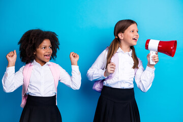 Two cheerful schoolgirls expressing creativity and fun with a megaphone against a vibrant blue...