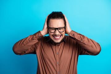 Confused young businessman in brown shirt holding his head with hands against a turquoise background