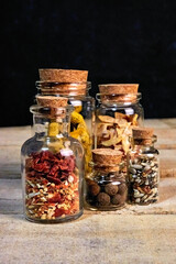 five transparent bottles with cork lids in which there are different spices on a dark background