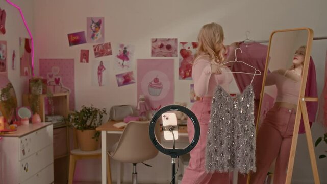 Young blonde fashion influencer filming haul on smartphone camera with ring light in her pink-themed bedroom