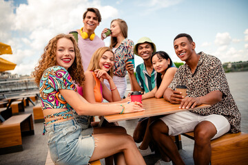 Cheerful young adults enjoying coffee and bonding outdoors on a warm summer day near a riverside area