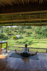 A young woman performs yoga on a bamboo terrace surrounded by vibrant jungle greenery during the...