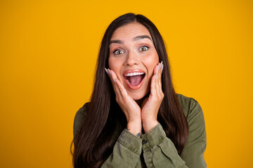 Excited young woman expressing joyful surprise on bright yellow background, wearing casual green...