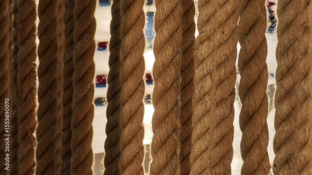 Poster light filtering through a curtain of thick ropes, creating a warm and textured pattern