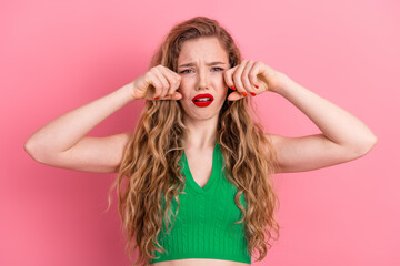 Young woman with long blonde hair wearing a green top posing on pink background showing a sad and...