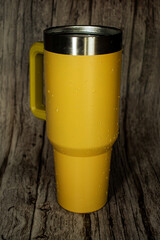 A vibrant yellow insulated travel mug with a black lid and metal straw, set against a rustic wooden background. Ideal for themes of sustainability, beverages on-the-go, and modern drinkware.