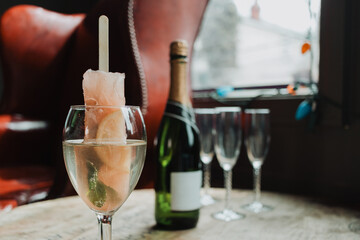 Grapefruit popsicle champagne cocktail in wine glass with mint leaf, champagne bottle and flutes on rustic wooden table in lounge setting