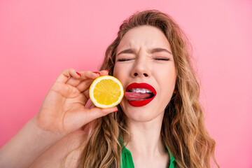 Youthful woman with long blonde hair enjoying a tangy lemon moment against a vibrant pink...