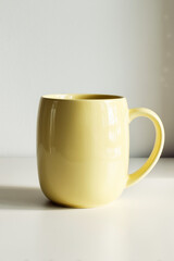 Obraz premium yellow ceramic mug on neutral countertop, minimalist design ideal for home decor or office setting, perfect for morning coffee, tea enthusiasts, aesthetic kitchenware enthusiasts