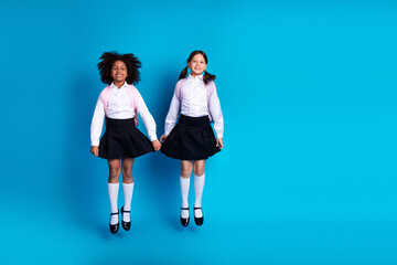 Smiling schoolgirls in uniform holding hands against a blue background indicating friendship and...