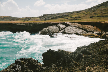 Waves crash against rocky coastline at a serene seaside location under bright blue skies
