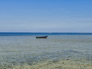 Solitary wooden boat floating on calm shallow sea with crystal clear water under bright blue sky....