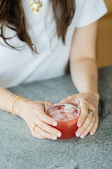 female torso leaning over grey kitchen counter holding glass of fizzy pink beverage