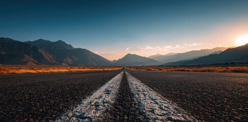 Empty asphalt road stretching into a mountain range at sunset