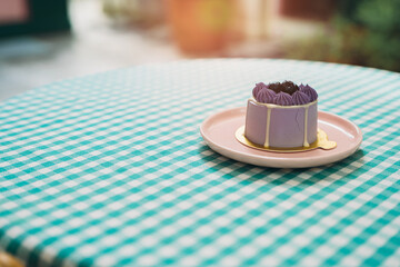 Cake in cafe. Elegant Purple Cake on Pink Plate Resting on Checkered Tablecloth in Sunlit Cafe Setting