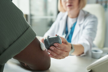 Middle aged Caucasian female doctor examining Black man's arm using glucose monitoring device...