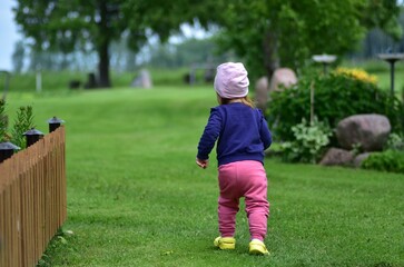 Confident little girl walking alone across a green lawn in the countryside. Rear view of a brave...