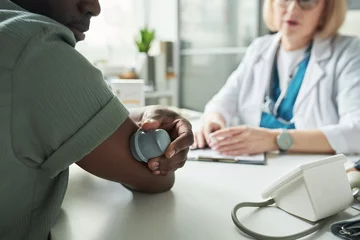 Gordijnen Black middle aged man checking blood glucose with medical device while sitting across from Caucasian middle aged female doctor in medical office during diabetes consultation © pressmaster