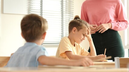 Beautiful teacher explaining test while caucasian boy doing classwork and listening explanation....